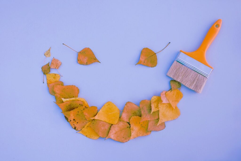 Brush paint with leaves emoji with a smile, creative autumn concept.